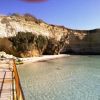 Una spiaggia con scogliere bianche e un pontile di legno che si affaccia su acque limpide.