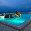 Piscina illuminata, lettini bianchi e mare sullo sfondo.
