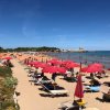Spiaggia sabbiosa con ombrelloni rossi e mare blu.