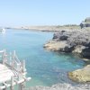 Scogliera rocciosa con mare calmo e barca lontana.