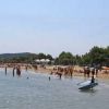 Spiaggia affollata con bagnanti e ombrelloni, alberi sullo sfondo.