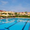 Piscina all'aperto con ombrelloni bianchi e lettini, edificio giallo sullo sfondo.