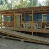 Veranda in legno con rampa d'accesso e sedie bianche sul patio.