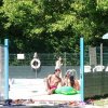 Persone si rilassano e giocano in piscina sotto gli alberi.