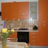Cucina con mobili arancioni, piano cottura, forno e fiori sul tavolo.
