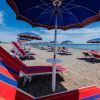 Spiaggia con ombrelloni e lettini rossi e blu, vista mare.