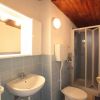 Un bagno con lavabo, toilette e doccia. Pareti piastrellate e soffitto in legno.
