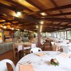 Sala ristorante con tavoli rotondi apparecchiati, grandi finestre e soffitto in legno.