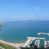 Vista di una baia con mare blu e un'isoletta. Un porto turistico è visibile sulla destra.