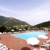 Piscina all'aperto circondata da lettini e ombrelloni bianchi, con montagne sullo sfondo.