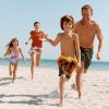 Famiglia corre sorridente sulla spiaggia di sabbia.