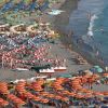 Una spiaggia affollata con file di ombrelloni colorati e persone che nuotano in mare.
