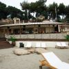 Spiaggia con lettini e bar in legno sullo sfondo.