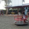Parco giochi con bimbi su giostra, altalene, e scivolo.