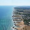 Veduta aerea di una costa con scogli e terreno erboso a destra.