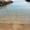 Spiaggia di sabbia dorata con mare calmo e rocce ai lati.