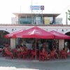 Persone al bar sotto ombrelloni rossi.