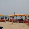 Spiaggia con ombrelloni gialli e rossi, persone rilassate e il mare sullo sfondo.