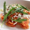 Ravioli al pomodoro con rucola e formaggio grattugiato, su un piatto bianco.