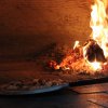 Pizza in un forno a legna, con fiamme visibili.