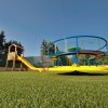 Parco giochi con scivolo giallo e giostra circolare colorata su prato artificiale.