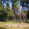 Una piramide di corde colorate in un'area giochi all'aperto circondata da alberi.