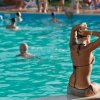 Persona seduta a bordo piscina, nuotatori in acqua.