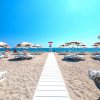 Passerella bianca su sabbia, circondata da lettini e ombrelloni, verso il mare.