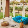 Terrazza con tenda, pouf blu e vista piscina.