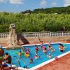 Bambini con cuffie colorate nuotano in una piccola piscina, circondati da istruttori.