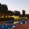 Piscina al tramonto con luci accese e sdraio arancioni.