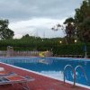 Piscina con sdraio arancioni e scivolo giallo, circondata da alberi e cielo nuvoloso.