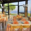 Ristorante con tavoli apparecchiati vicino a finestre, vista sul mare e giardino.