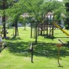 Parco giochi su prato verde con scivolo e altalene.