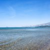 Spiaggia con acqua cristallina, monti in lontananza e cielo blu chiaro.