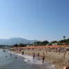 Bagnanti sulla riva di una spiaggia con montagne sullo sfondo.
