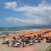 Spiaggia con ombrelloni arancioni e persone che prendono il sole, mare sullo sfondo.