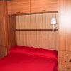 Camera da letto con mobili in legno, letto matrimoniale con coperta rossa e lampada su mensola.