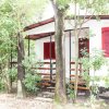 Piccola casa bianca con finestre rosse e veranda, circondata da alberi verdi.