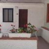Un patio con muri bianchi, fioriere con fiori rossi e una porta di legno marrone.