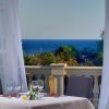 Tavolo apparecchiato con vista mare, tende bianche.