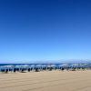 Lunga spiaggia con file di sedie e ombrelloni.