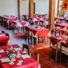 Sala ristorante con tavoli apparecchiati con tovaglie rosse e decorazioni floreali.