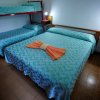 Letto matrimoniale con copriletto azzurro e letto a castello, lampade accese sui comodini.