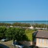 Vista sul mare con una casa in primo piano, alberi e auto parcheggiate lungo la strada.