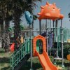 Scivolo arancione in un parco giochi con palme.