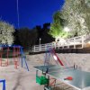 Parco giochi illuminato di sera con altalene e tavolo da ping pong.