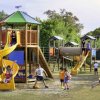 Parco giochi con bambini su scivoli e altalene.