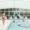 Interno di una piscina coperta con persone che nuotano e una donna sul bordo.