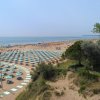 Spiaggia con file ordinate di ombrelloni e lettini, persone godono del sole vicino all'oceano.